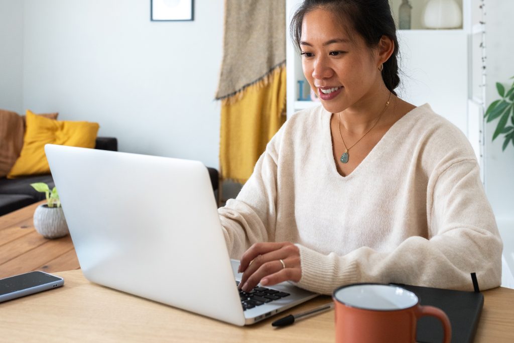 Happy Asian female entrepreneur working using laptop. Smiling Chinese woman working with computer at home office. Vertical. Technology concept.